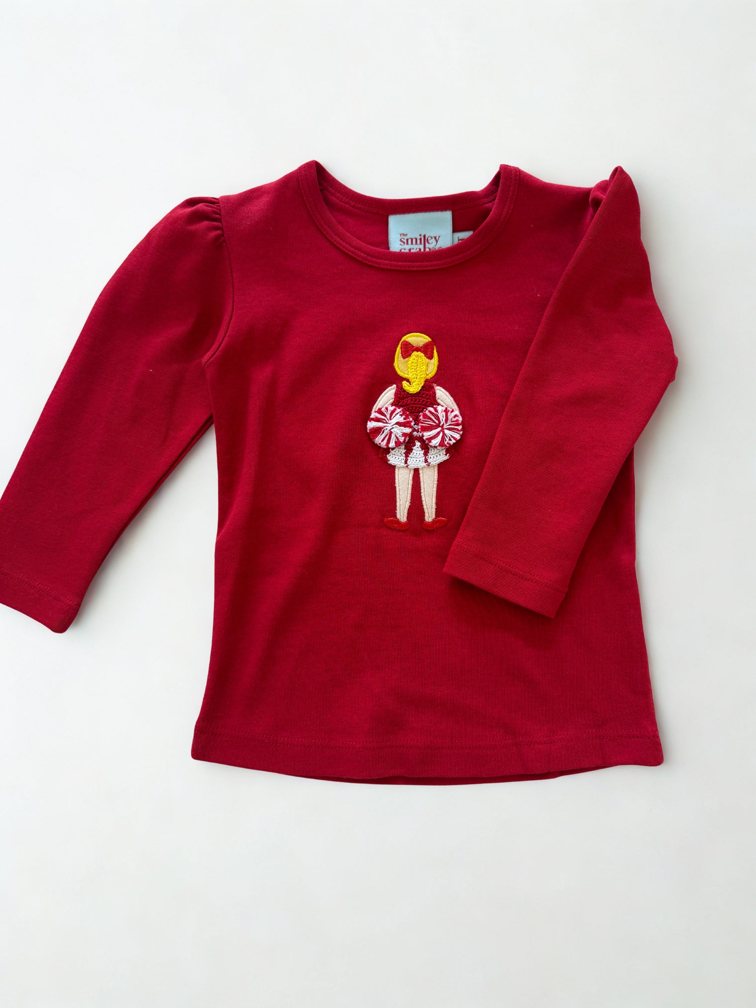 Red Shirt with a Cheerleader Holding Pom Pom’s Behind Her Back